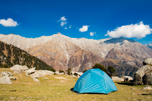 A single blue tent seen against Dhaulahaar peaks of Himalayas in Triund. Sunny day whit some clouds. Dharamshala, Himachal Pradesh. India